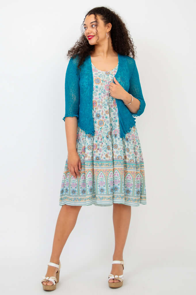 Woman smiling in floral tiered dress, teal cardigan, and wedge sandals