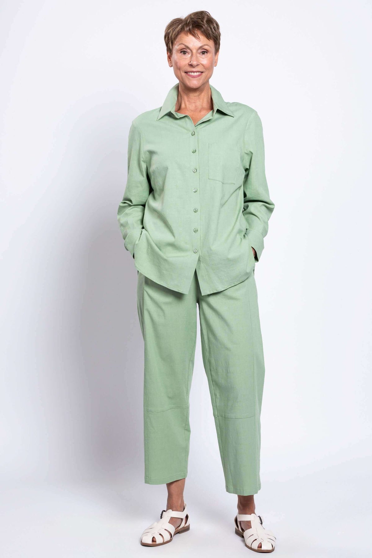 Woman smiling with hands in pockets, dressed in a sage green shirt and pants set