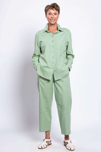 Woman smiling with hands in pockets, dressed in a sage green shirt and pants set