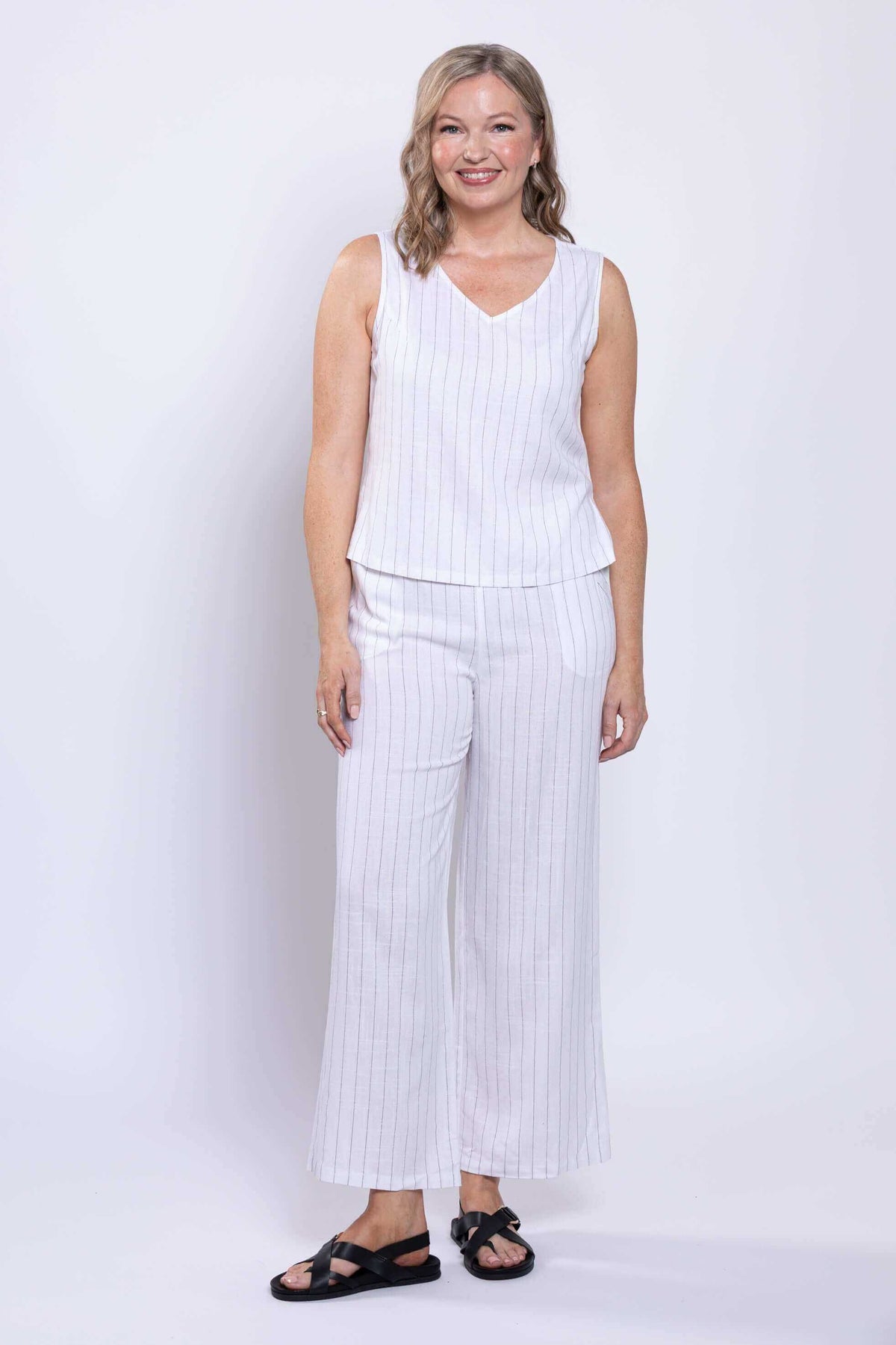 Woman smiling in a white striped sleeveless V-neck tank and pants