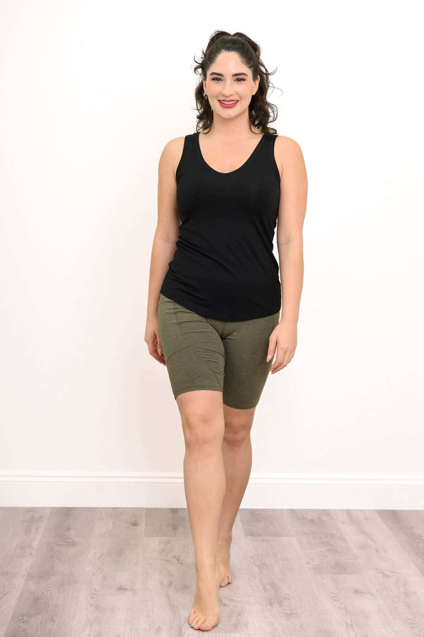Woman wearing olive green bike shorts and a black tank top standing barefoot