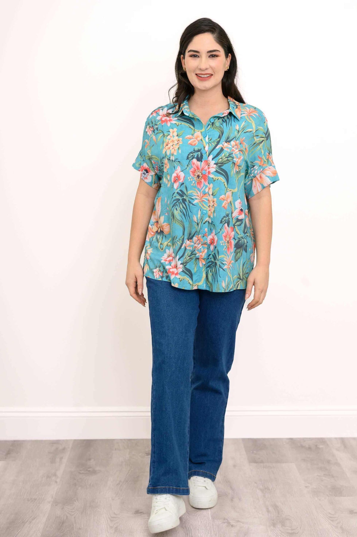 Woman standing in a turquoise floral blouse and jeans, front view