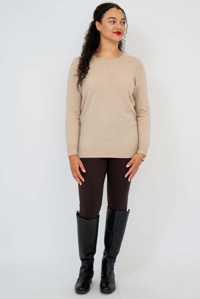 Woman standing in beige sweater, brown pants, and black boots