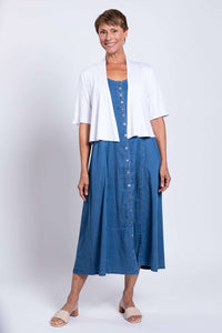 Woman standing in blue Tencel denim maxi dress layered with white cardigan