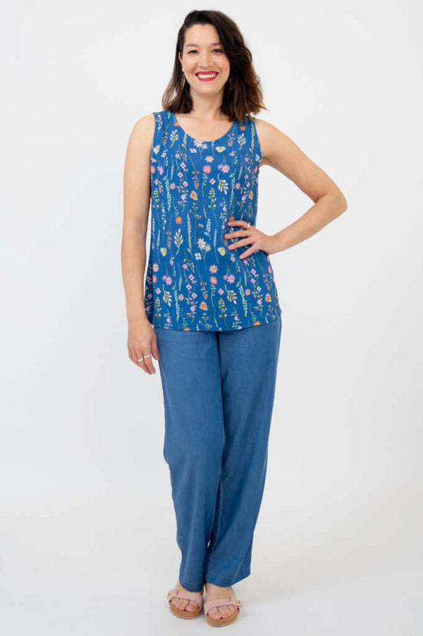 Woman in full-length blue floral tank and blue pants, standing, one hand on hip
