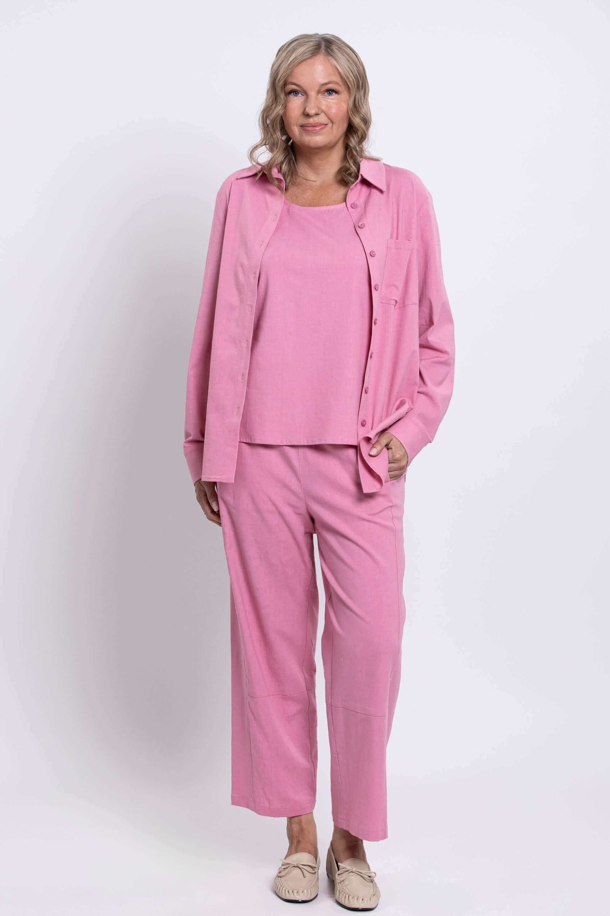 Woman in a pink shirt and pants outfit, standing with one hand in pocket, full body front view