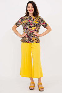 Woman posing in a bright botanical print tee and wide yellow pants, hands on hips