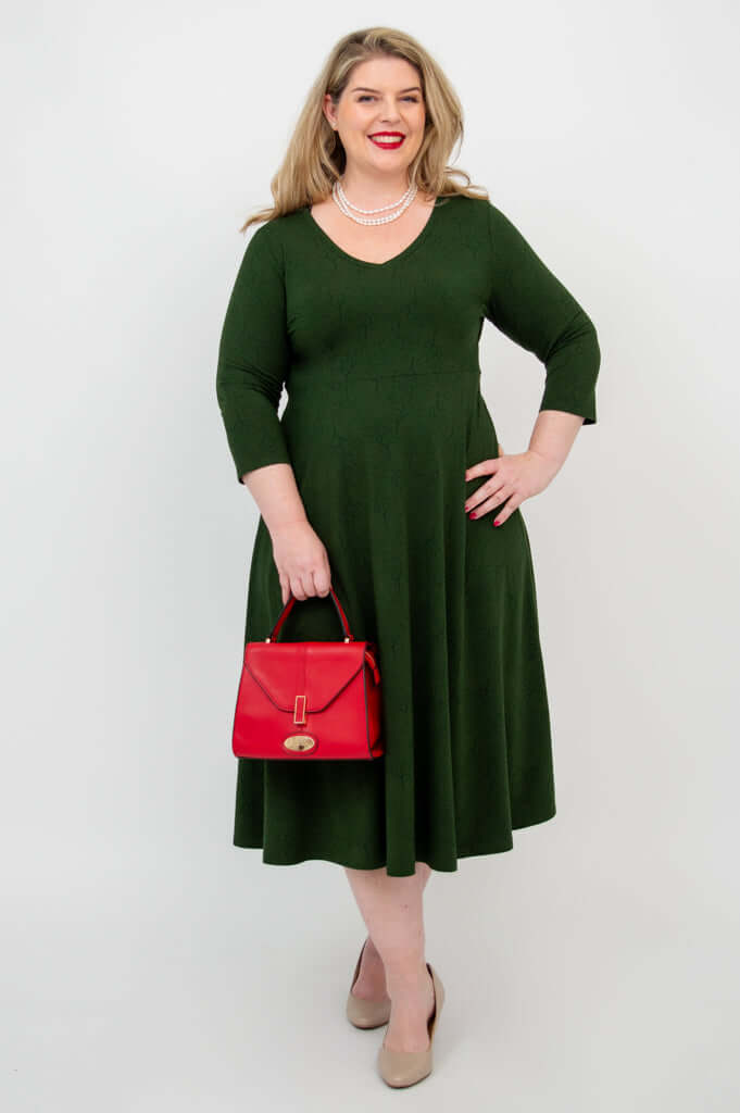 Woman in green midi dress accessorized with a red handbag and pearl necklace