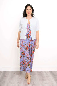 Woman in a light cardigan over a purple floral jumpsuit with red flowers
