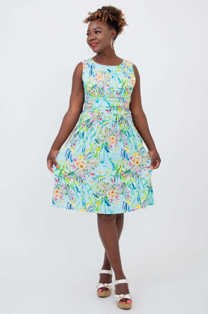 Woman twirling in blue floral ruched dress with a vibrant print
