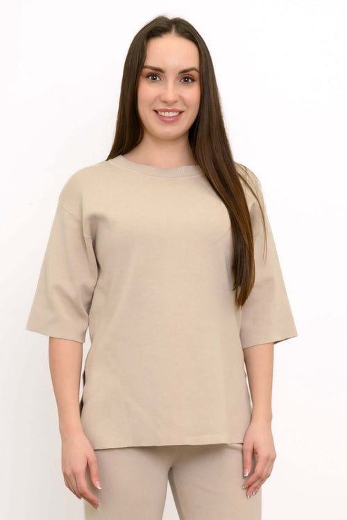 Woman modeling a monochromatic beige lounge outfit featuring a short sleeve knit top and knit trousers.