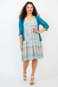 Woman wearing a floral tiered dress with teal cardigan and white wedge sandals