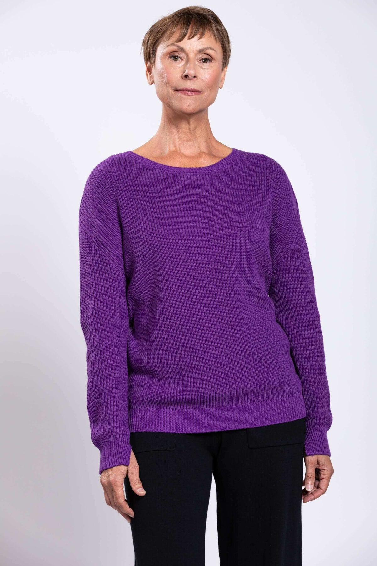Woman wearing a relaxed purple shaker stitch sweater with black pants, front view