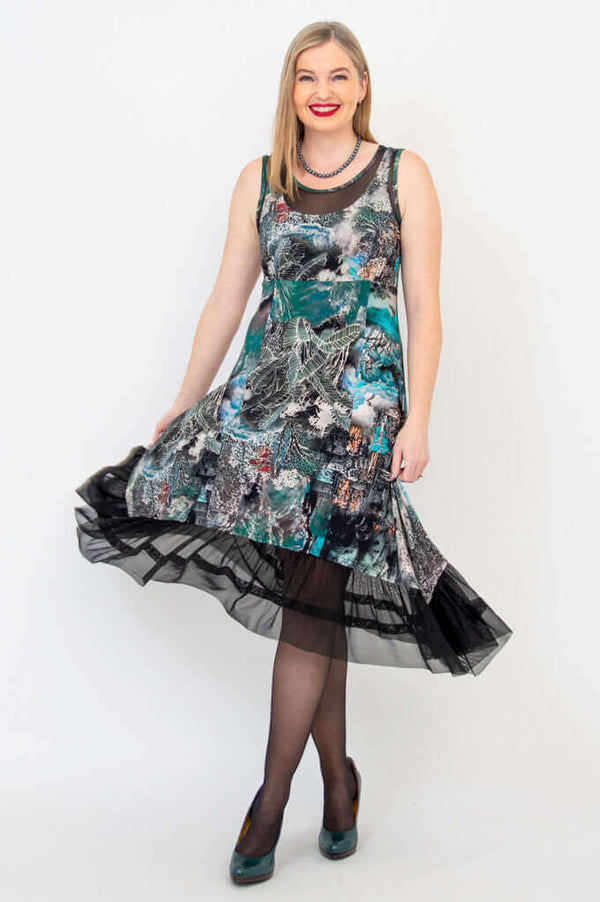 Woman wearing a sleeveless printed dress with mesh hem, holding skirt to side
