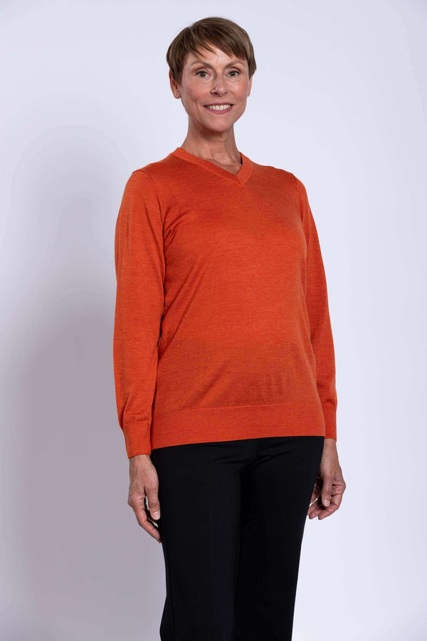 Woman wearing an orange V-neck merino wool sweater, front view, smiling