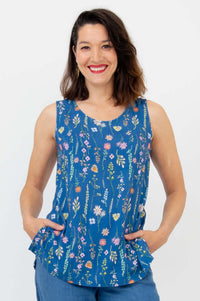 Woman wearing blue floral scoop neck sleeveless tank top, hands in pockets, smiling