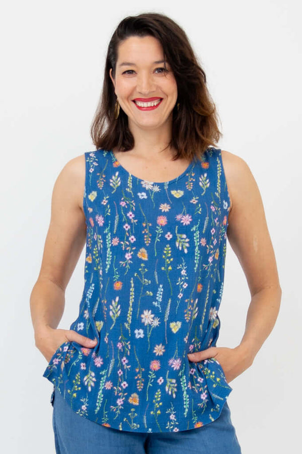 Woman wearing blue floral scoop neck sleeveless tank top, hands in pockets, smiling