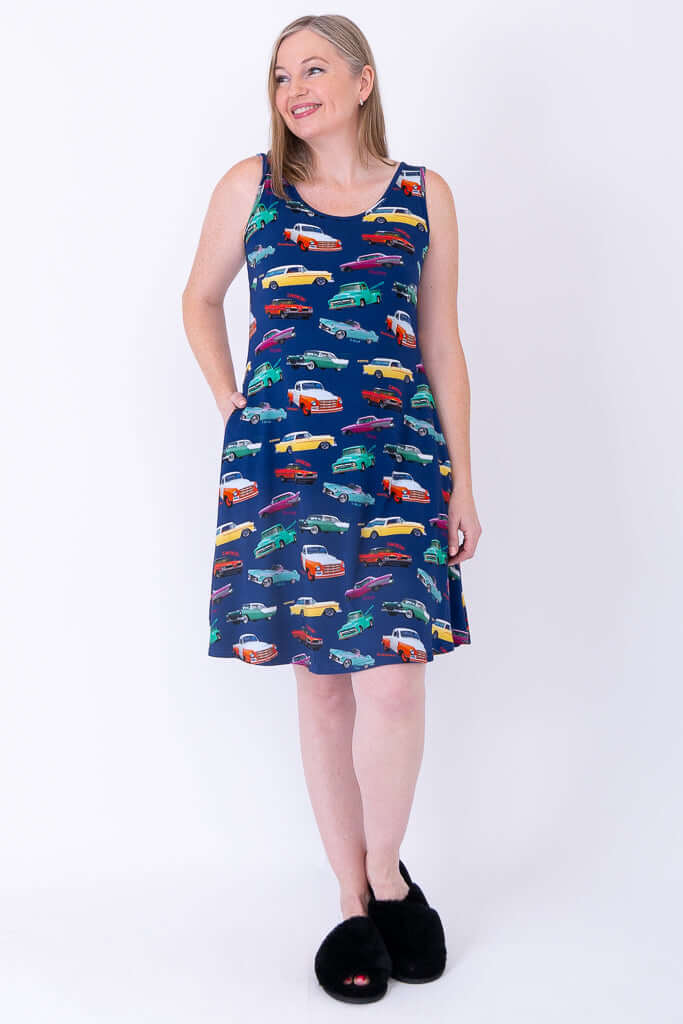 Woman in sleeveless vintage car patterned dress, hands in pockets, looking sideways