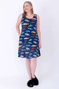 Woman in sleeveless vintage car patterned dress, hands in pockets, looking sideways
