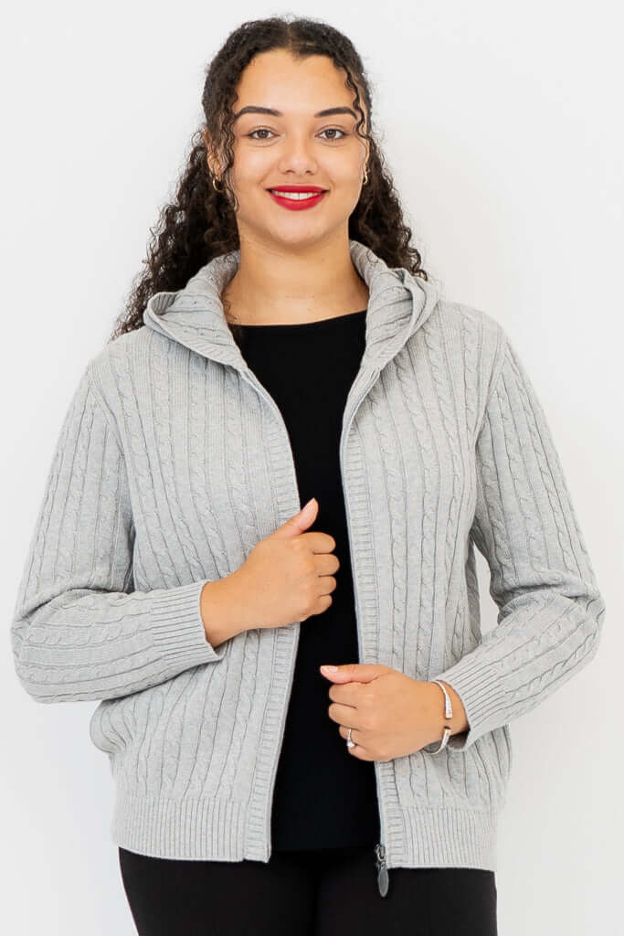 Woman wearing a light grey cable knit zip-up hoodie with a hood, hand on zipper