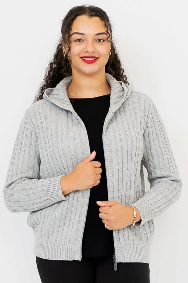 Woman wearing a light grey cable knit zip-up hoodie with a hood, hand on zipper