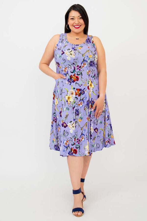 Woman wearing a sleeveless lilac floral A-line dress with pockets, standing and smiling
