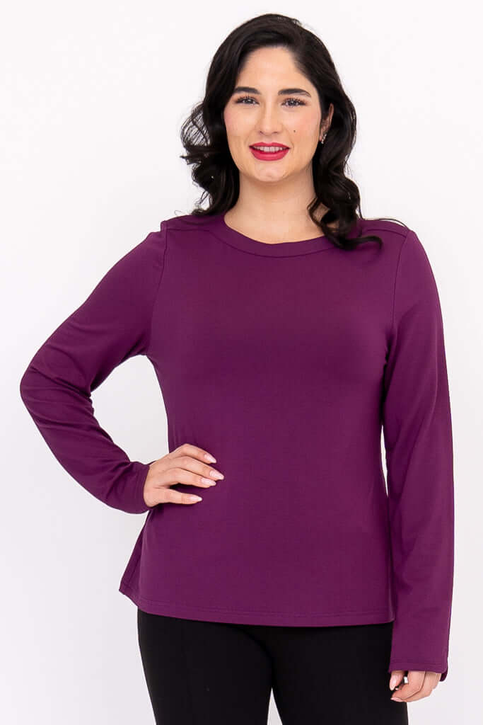 Woman wearing a long sleeve purple boat neck top with hands on hips