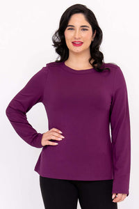 Woman wearing a long sleeve purple boat neck top with hands on hips