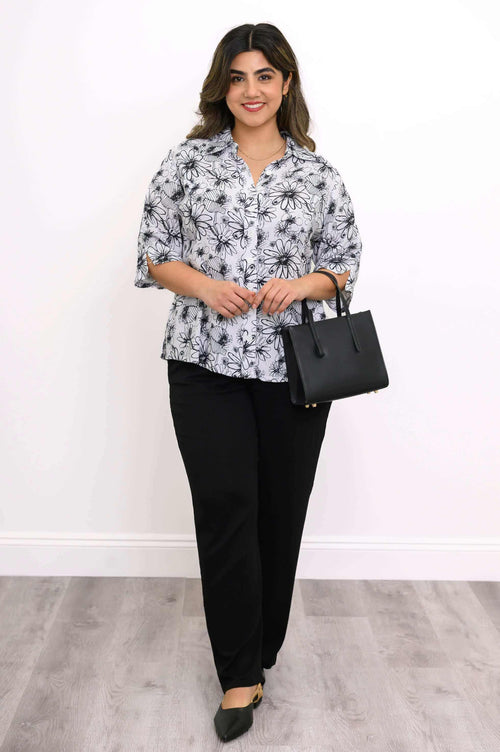 Woman holding a black handbag and wearing a floral bamboo linen blouse with black pants