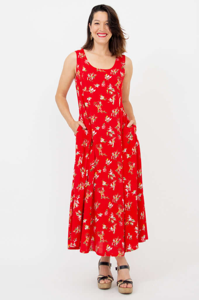 Smiling woman in a red sleeveless floral maxi dress with hands in pockets