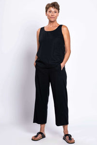 Woman standing with hands in pockets wearing black tank top and pants