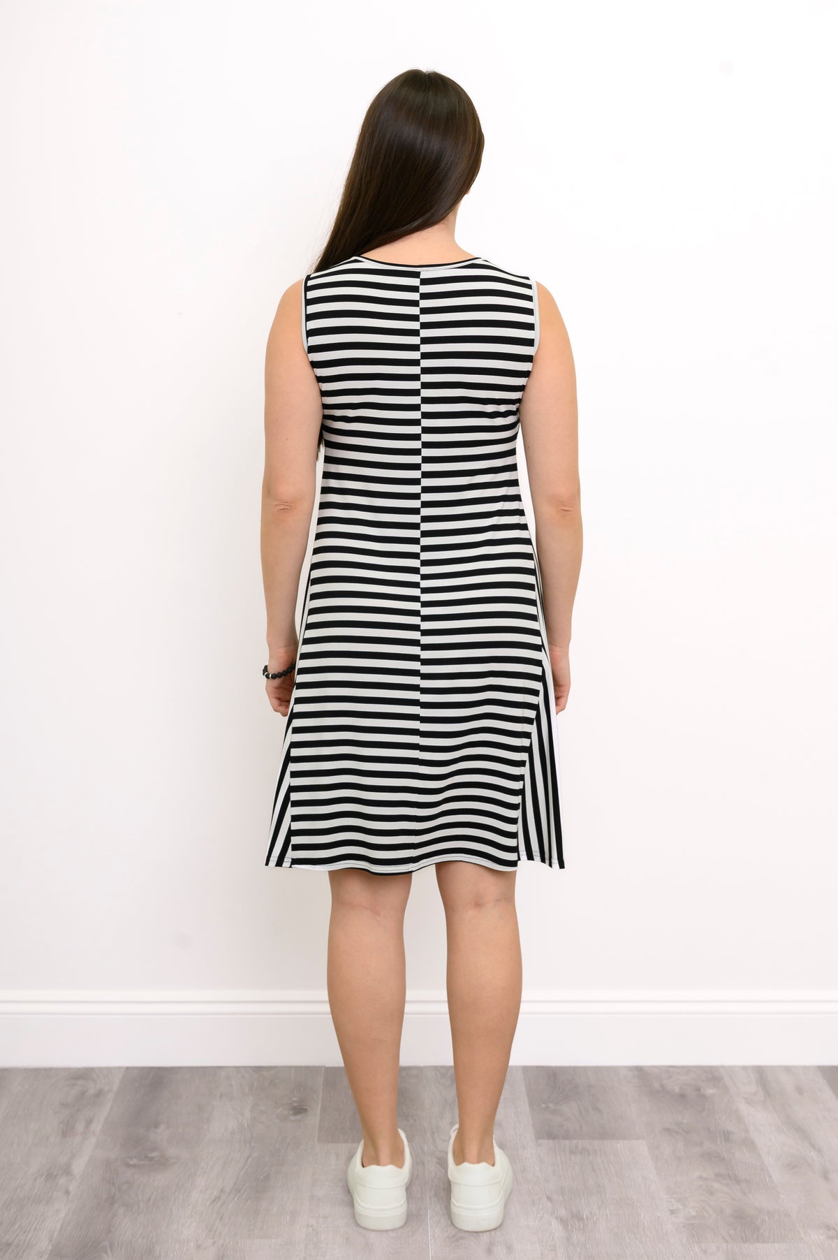 Back view of a woman wearing a sleeveless black and white striped bamboo dress with a round neckline and knee-length hem.