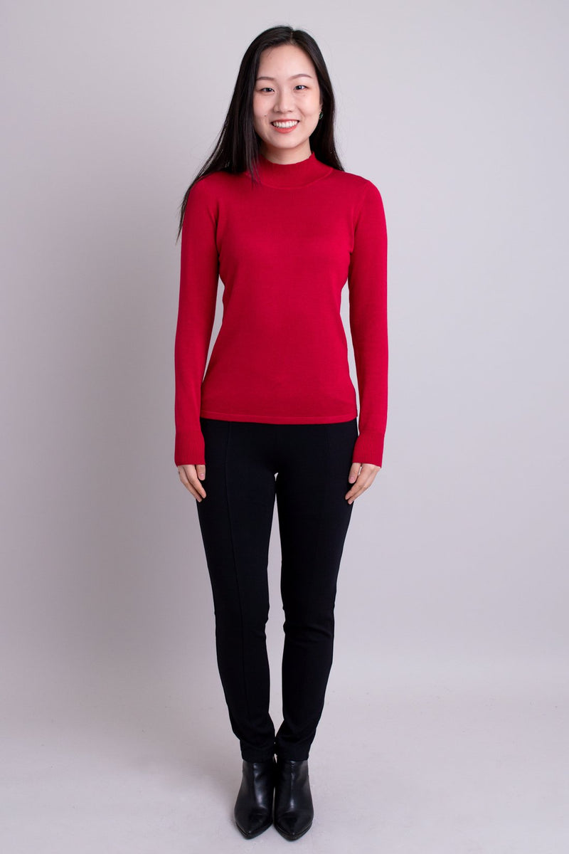 Women's red long-sleeve mock neck sweater worn with black pants. Made with sustainable and natural fibers, fair-trade.