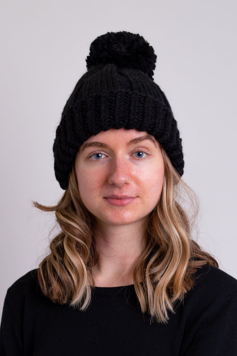 Women's black knit toque wool hat with pompom.